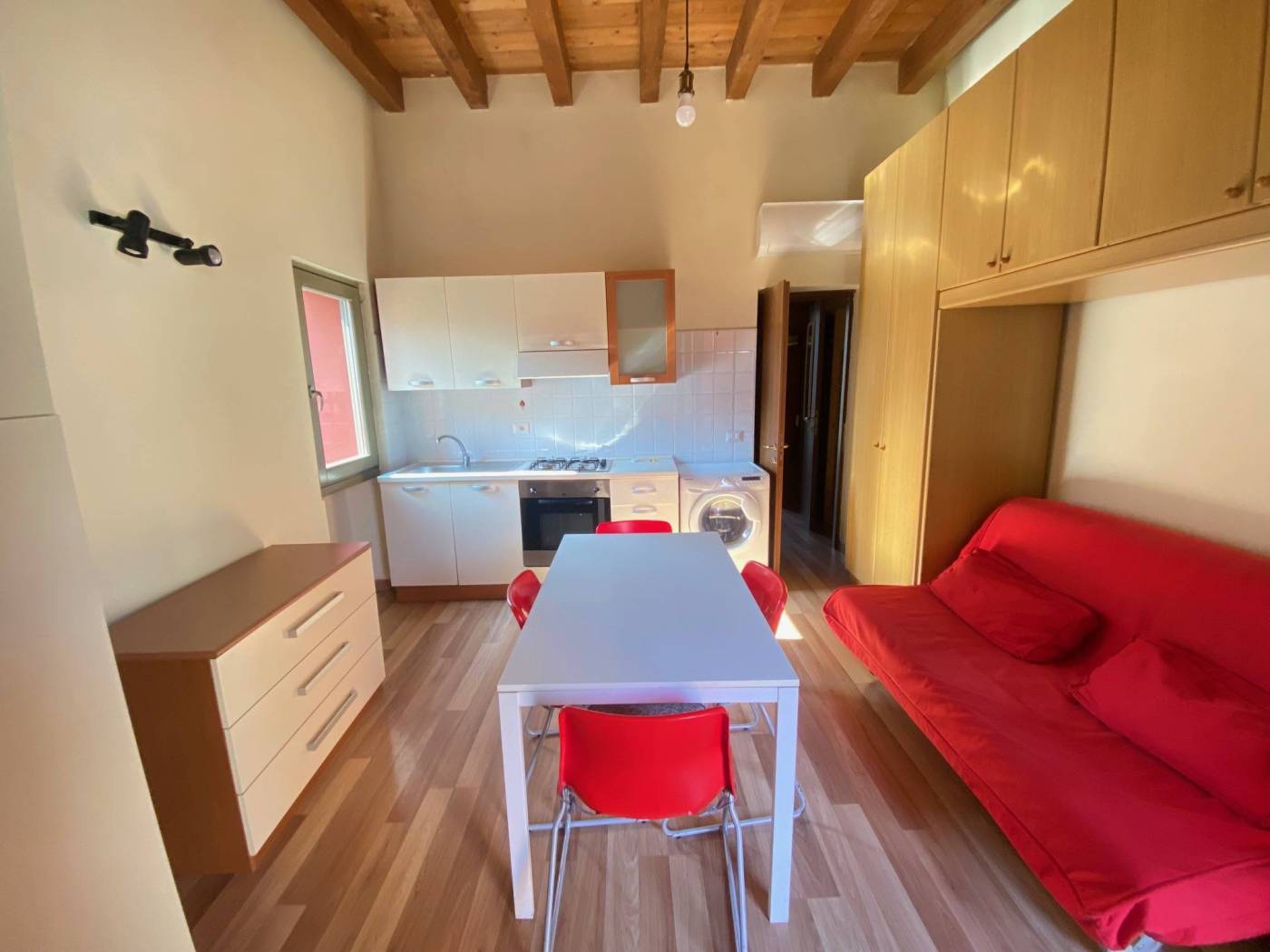 Bilocale in contesto di cortile composto da soggiorno arredato con armadio a ponte e divano letto, con parete cottura a vista, disimpegno, camera 
